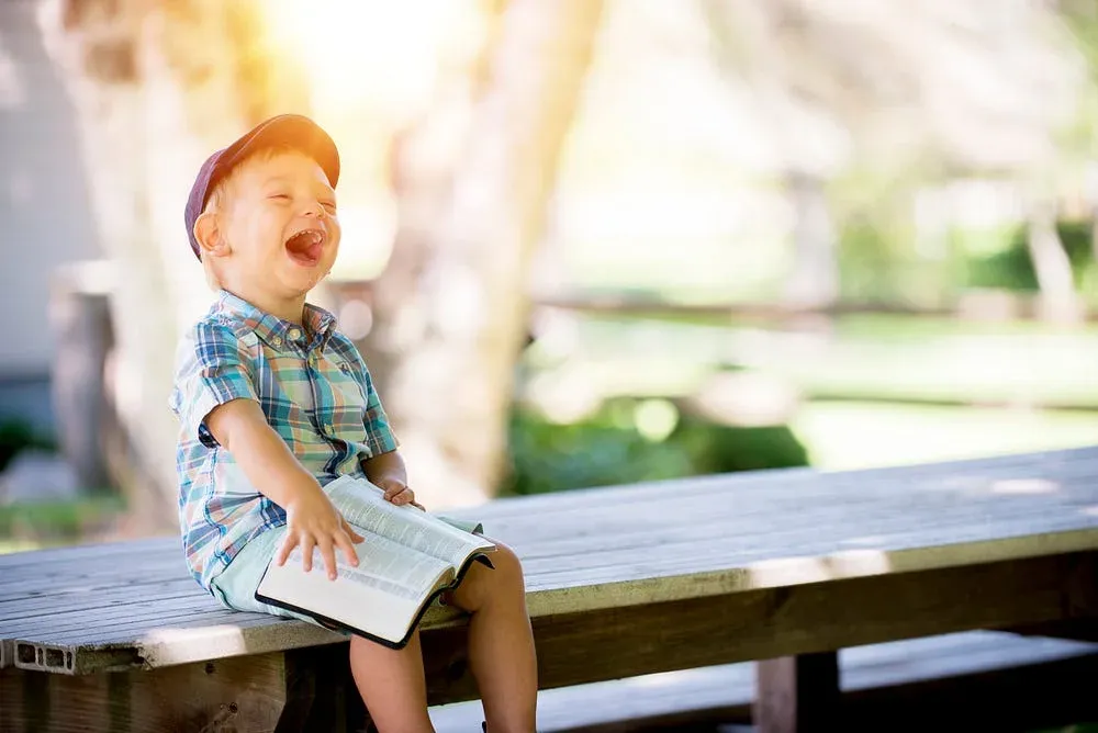 Laughing child holding an open book on a wooden bench